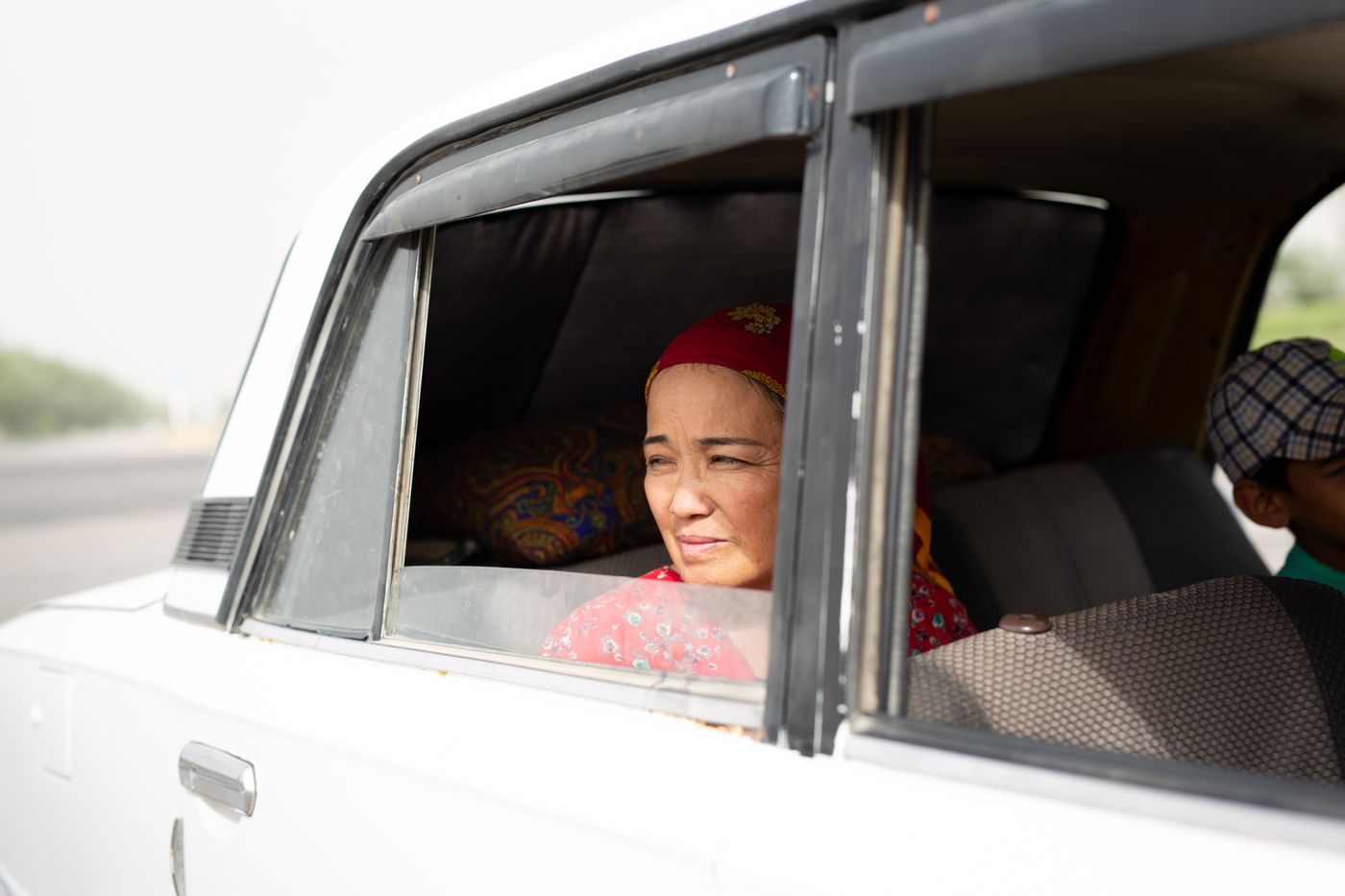 A woman in a red headscarf looks out of a car window