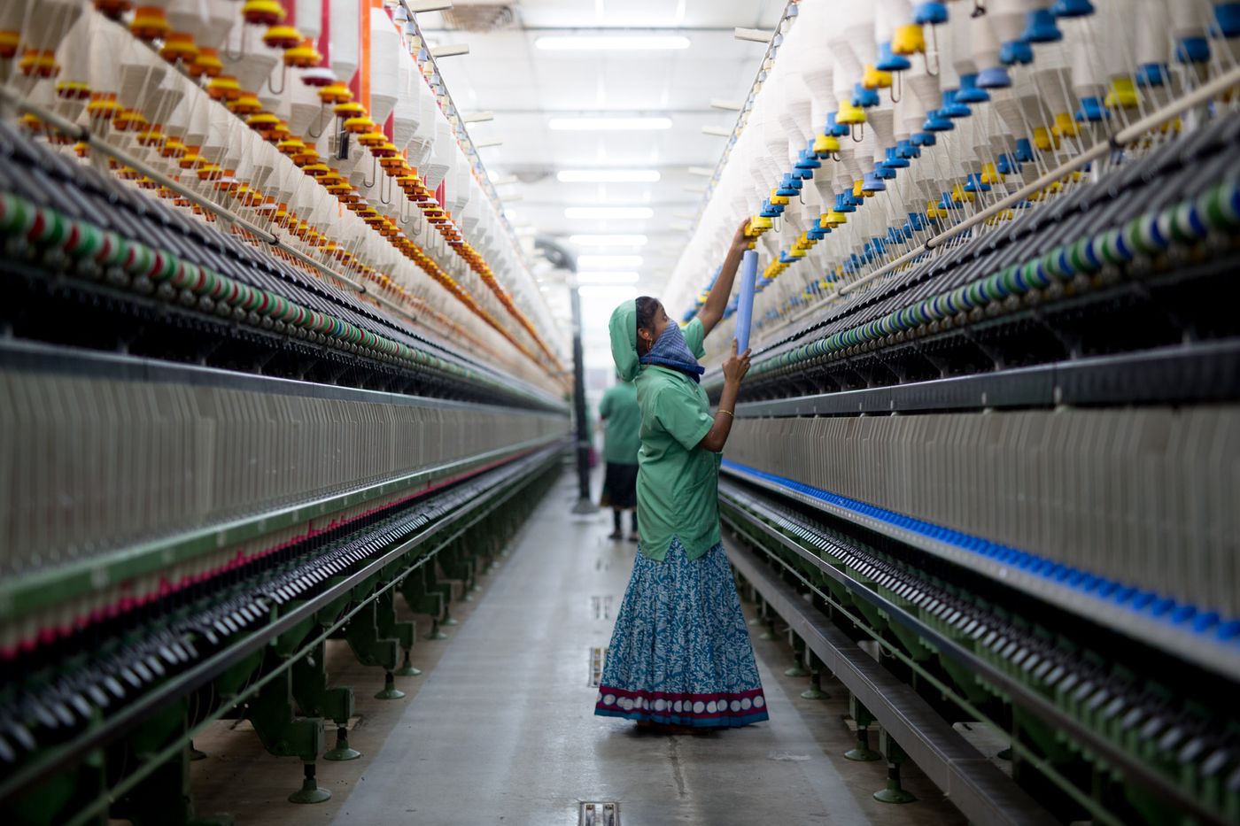 A worker in a green uniform tends a spinning machine between rows of yarn bobbins