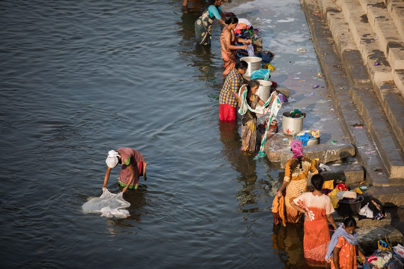 Women washing clothes and fabric on the stone steps of a river