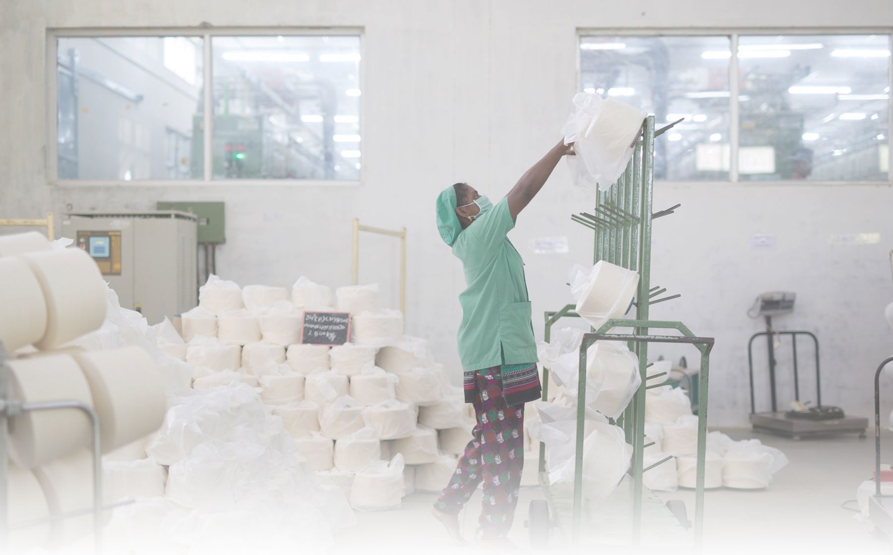 A worker in a green uniform hangs cones of cotton yarn on a rack in a spinning mill